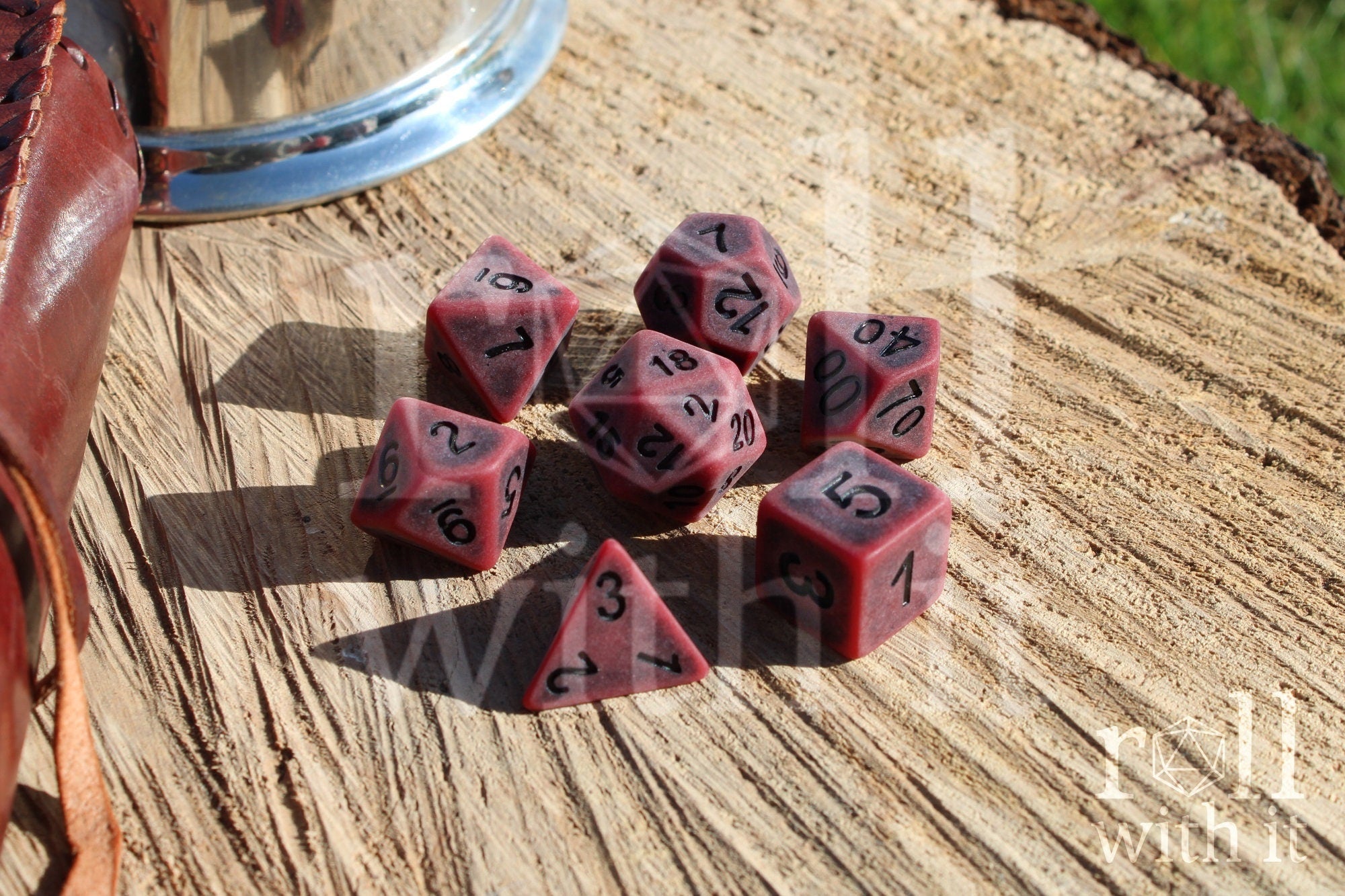 Matte red polyhedral roleplaying dice with a worn look with black lettering set on a wooden surface