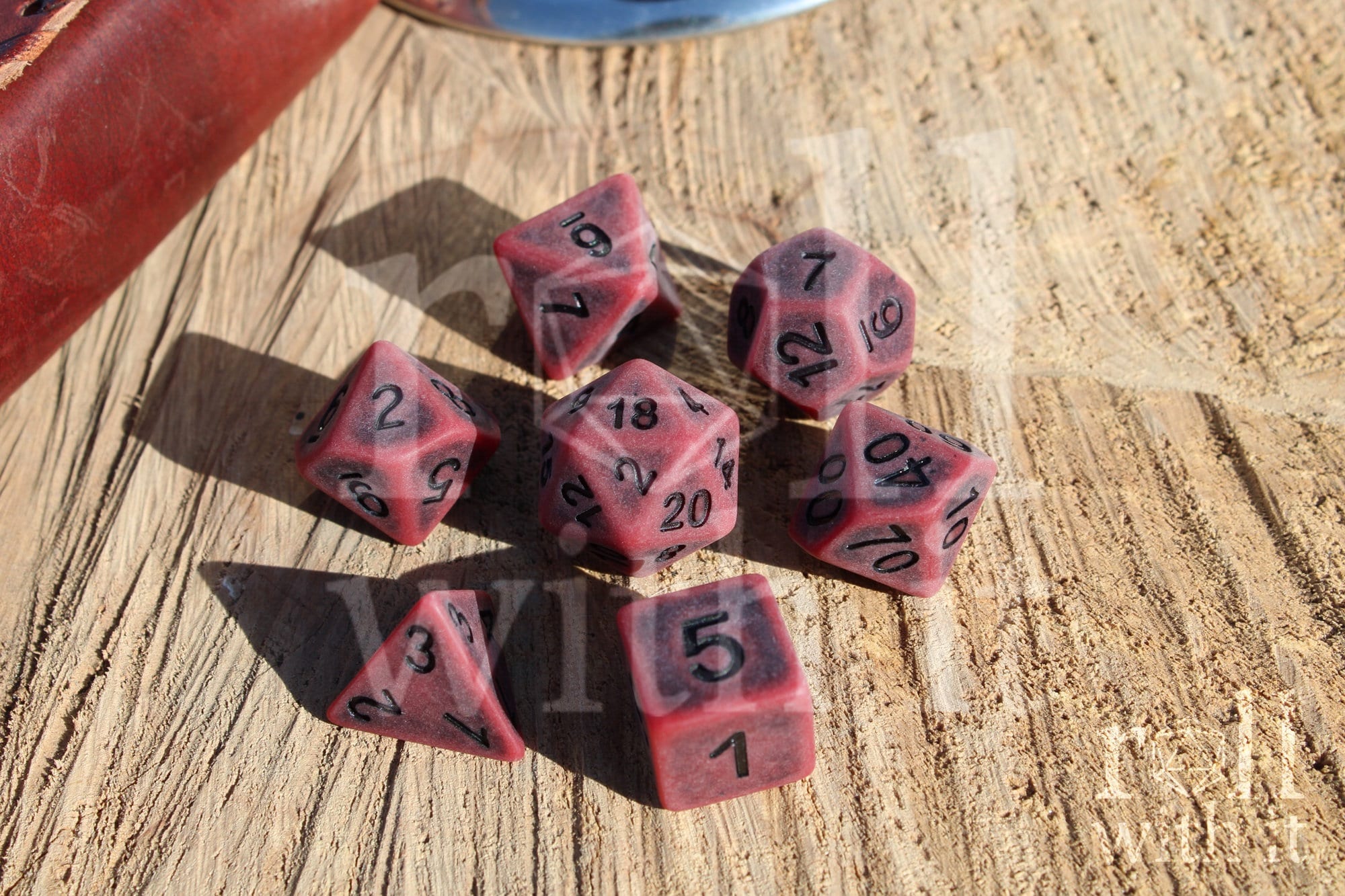 Matte red polyhedral roleplaying dice with a worn look with black lettering set on a wooden surface