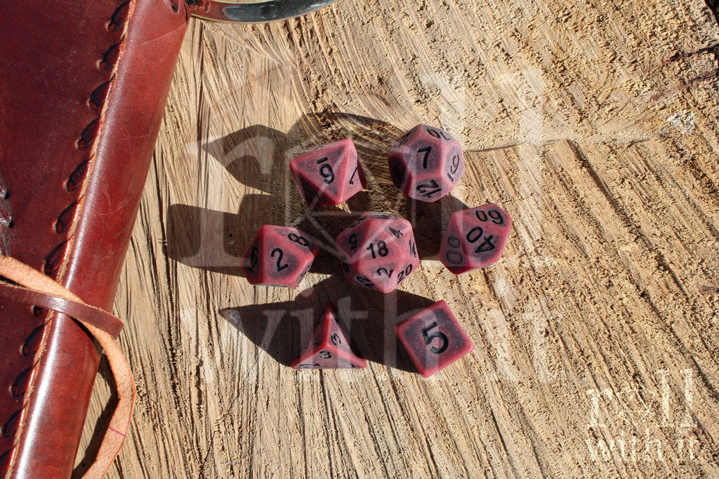 Matte red polyhedral roleplaying dice with a worn look with black lettering set on a wooden surface