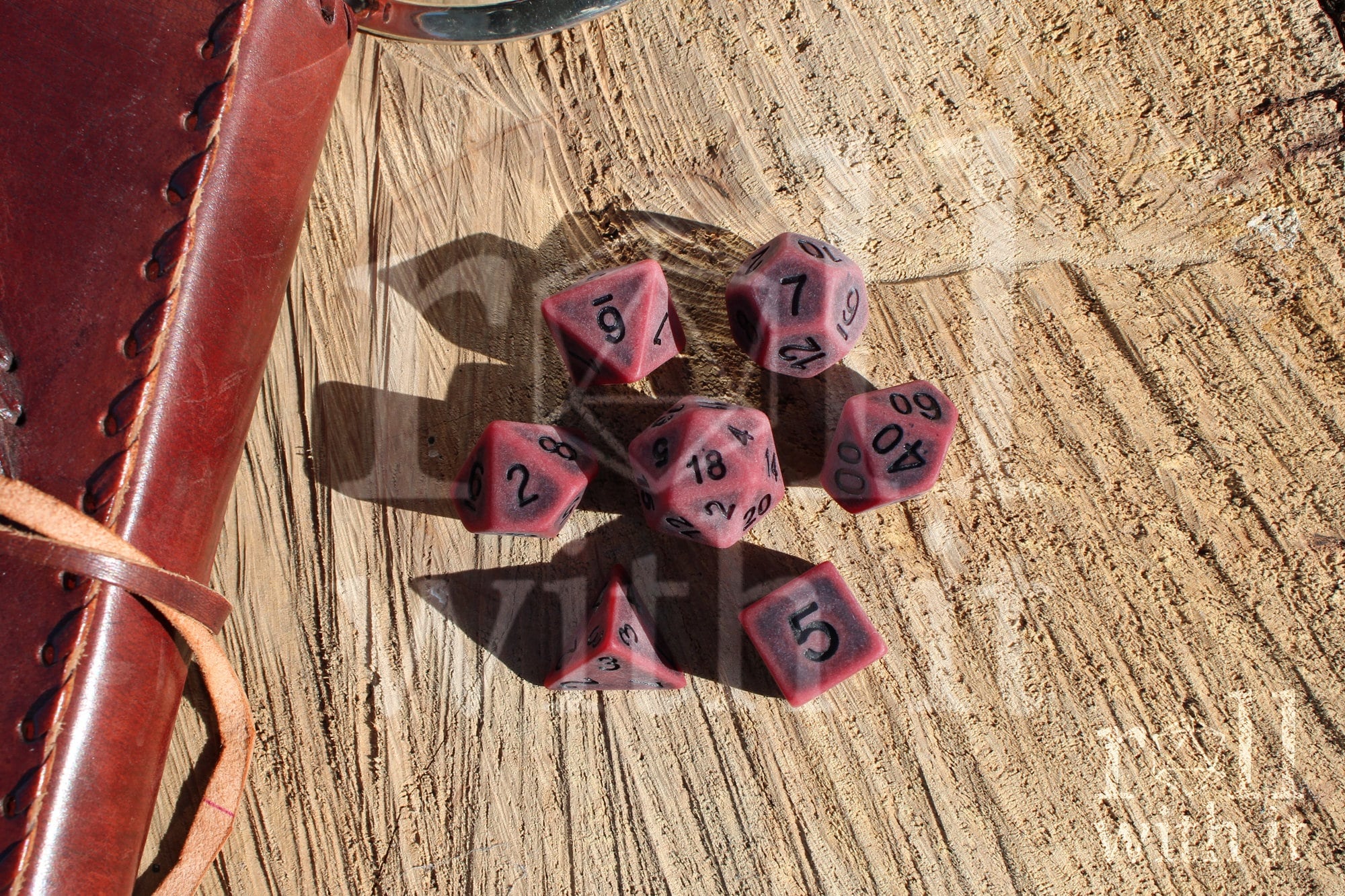 Matte red polyhedral roleplaying dice with a worn look with black lettering set on a wooden surface