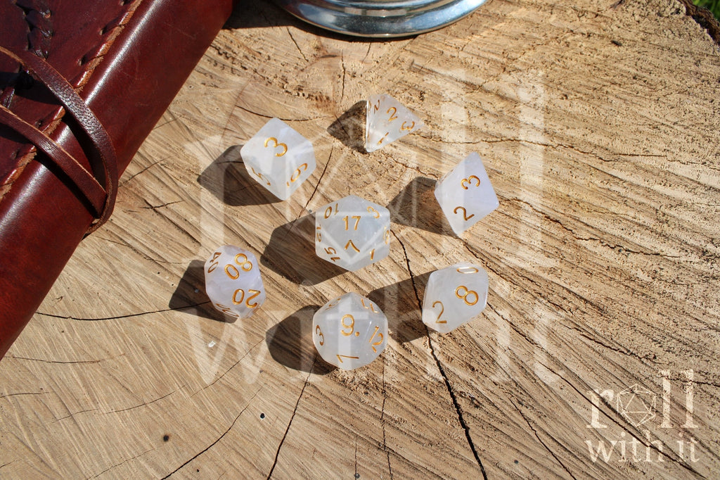 A set of polyhedral grey and silver roleplaying dice with gold numbers on a wooden 