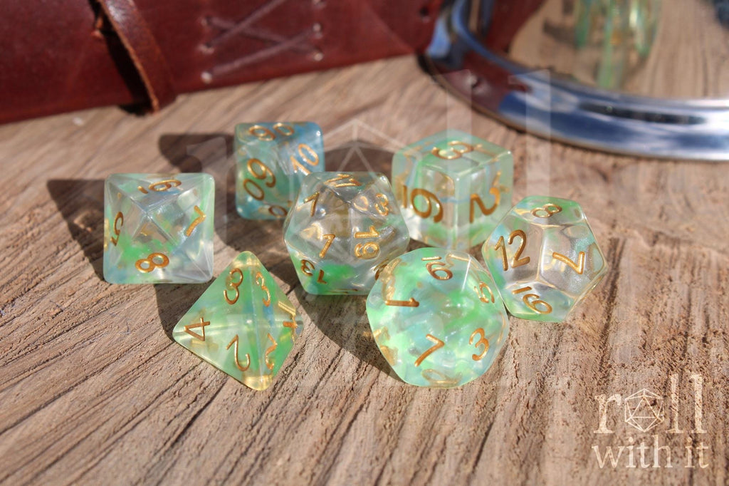 Set of green and pale blue clear polyhedral dice with gold numbers on a wooden surface