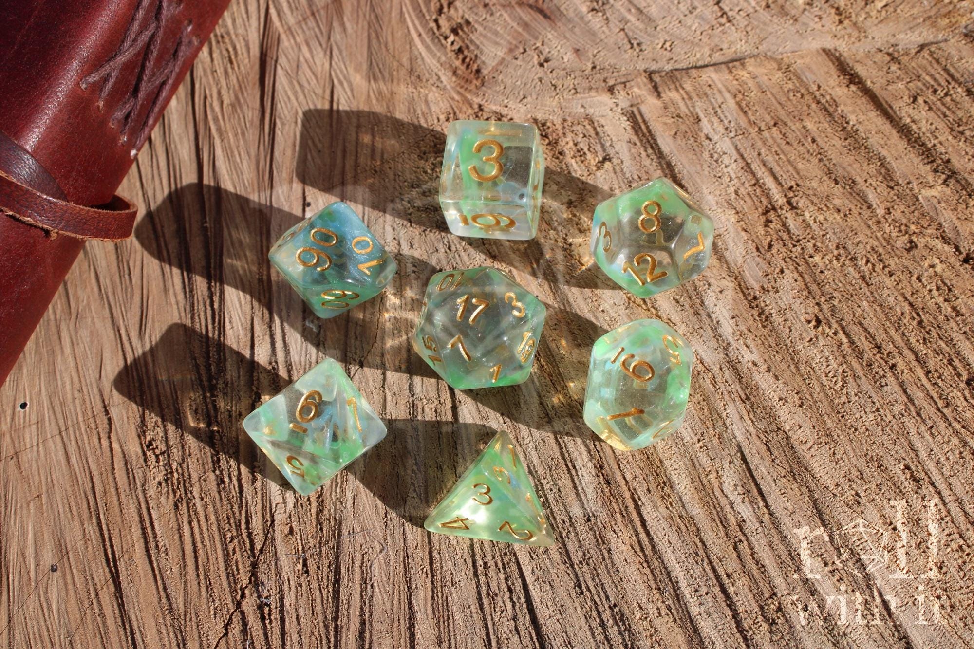 Set of green and pale blue clear polyhedral roleplaying dice with gold numbers on a wooden surface