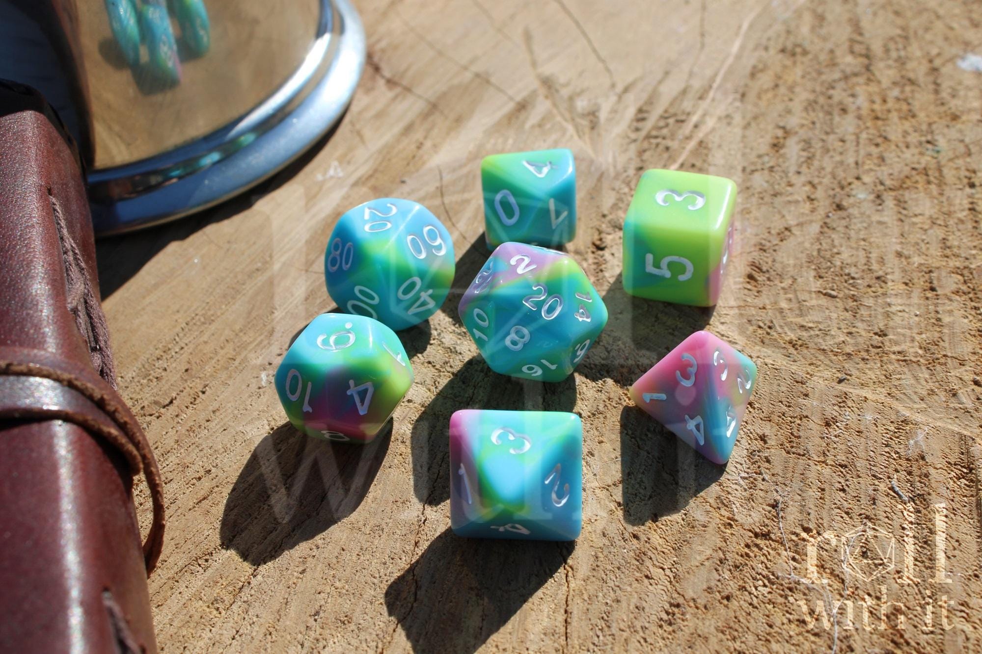 Colourful pastel rainbow polyhedral dice set on a wooden surface with a leather journal in the background 