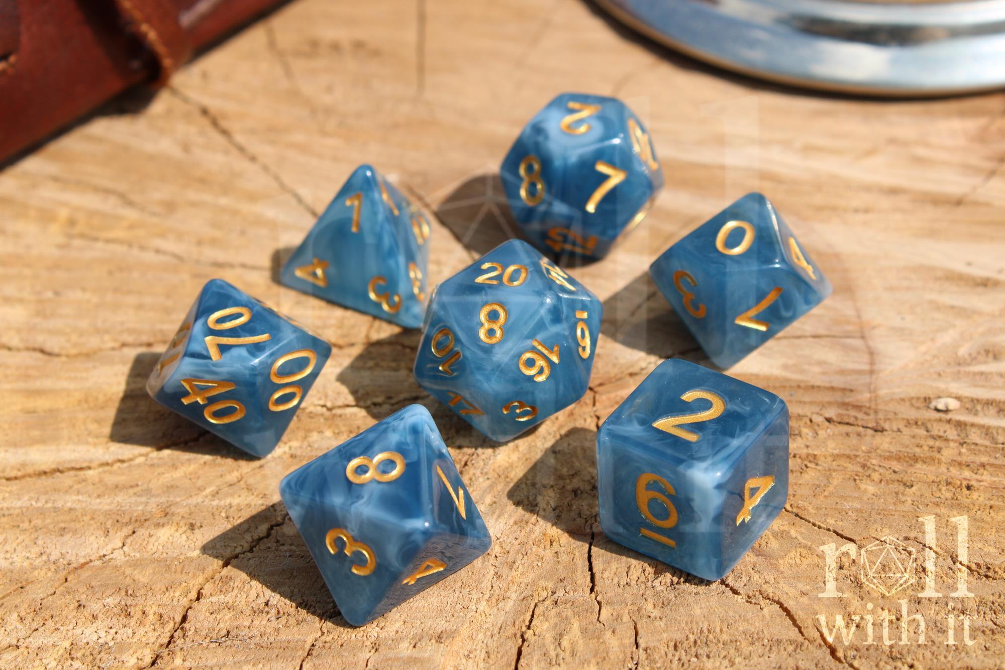 Set of jade blue translucent polyhedral roleplaying dice with gold numbering on a wooden base.