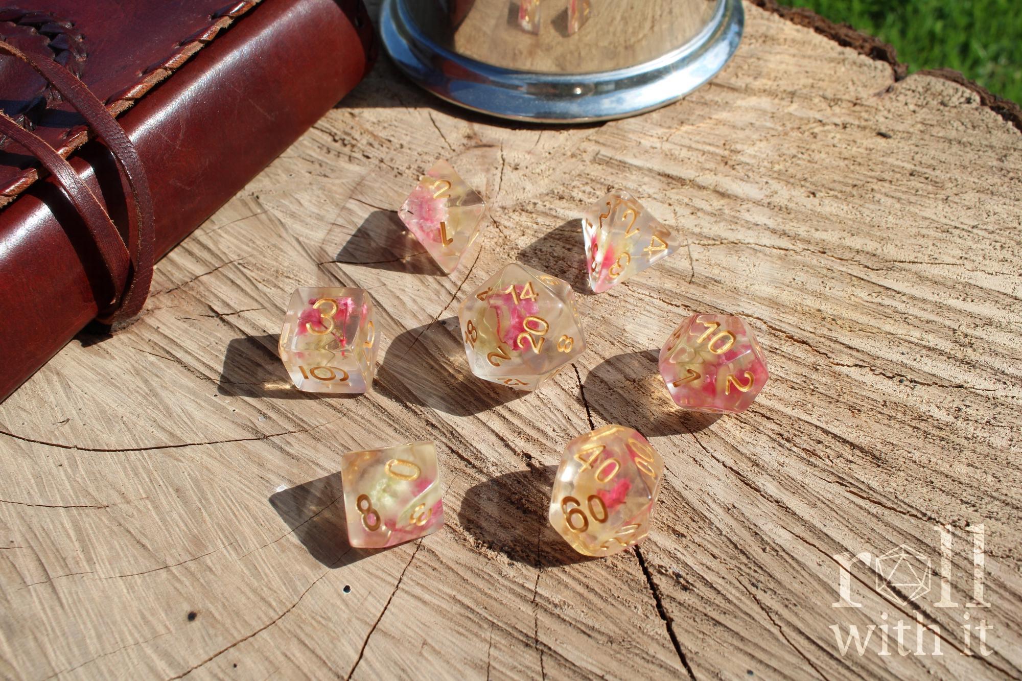Set of transparent polyhedral DND dice with pink yellow flowers inside with gold numbers on a wooden surface