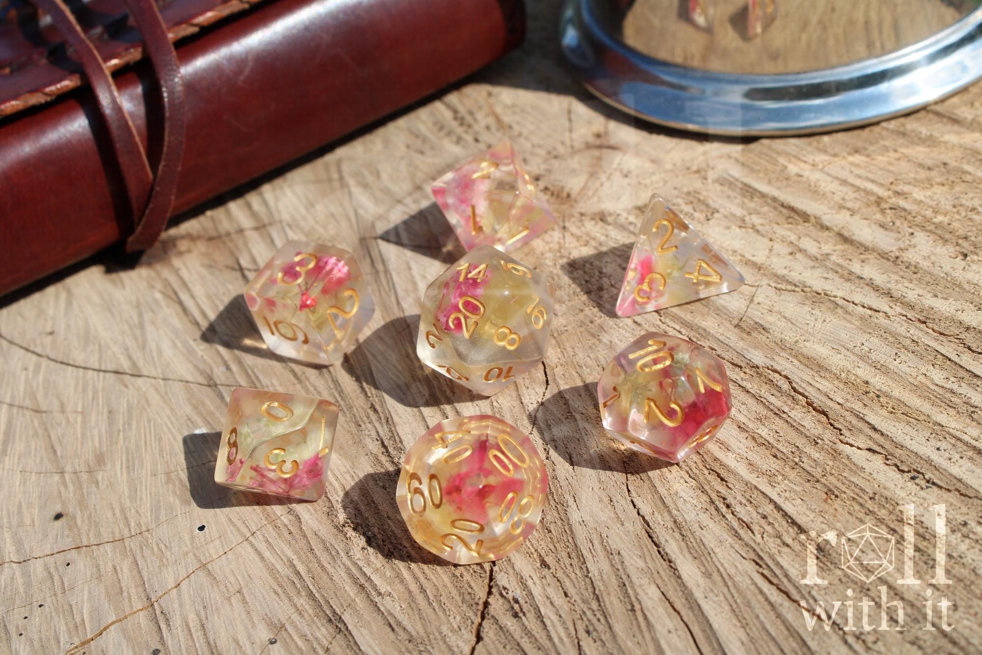 Set of transparent DND dice with pink  yellow flowers inside with gold numbers on a wooden surface
