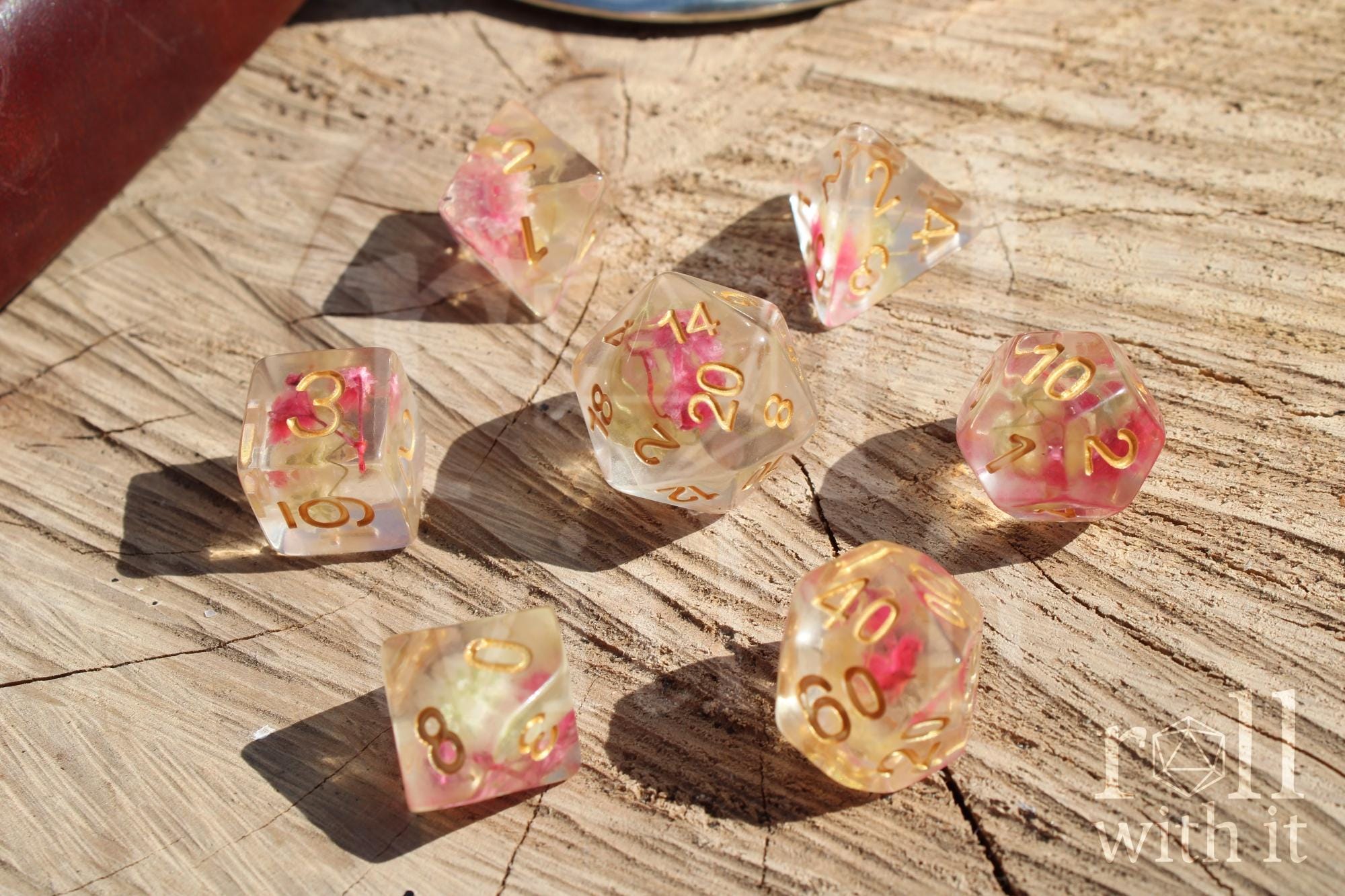Set of transparent polyhedral roleplaying dice with pink yellow flowers inside with gold numbers on a wooden surface