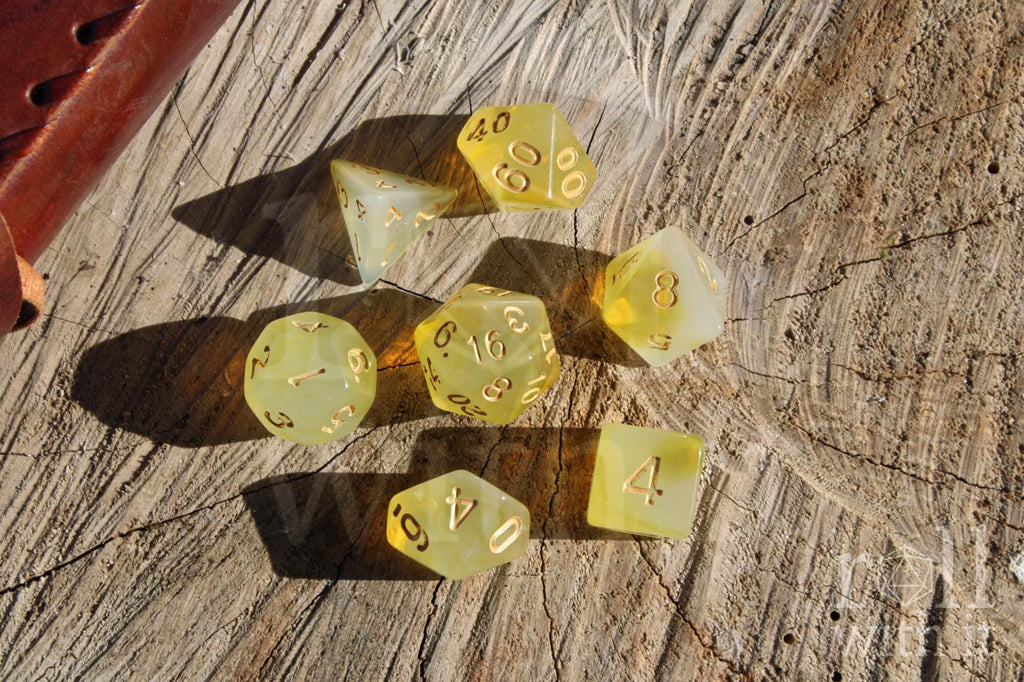 Set of translucent sherbet yellow polyhedral roleplaying dice with gold numbers on a wooden surface.