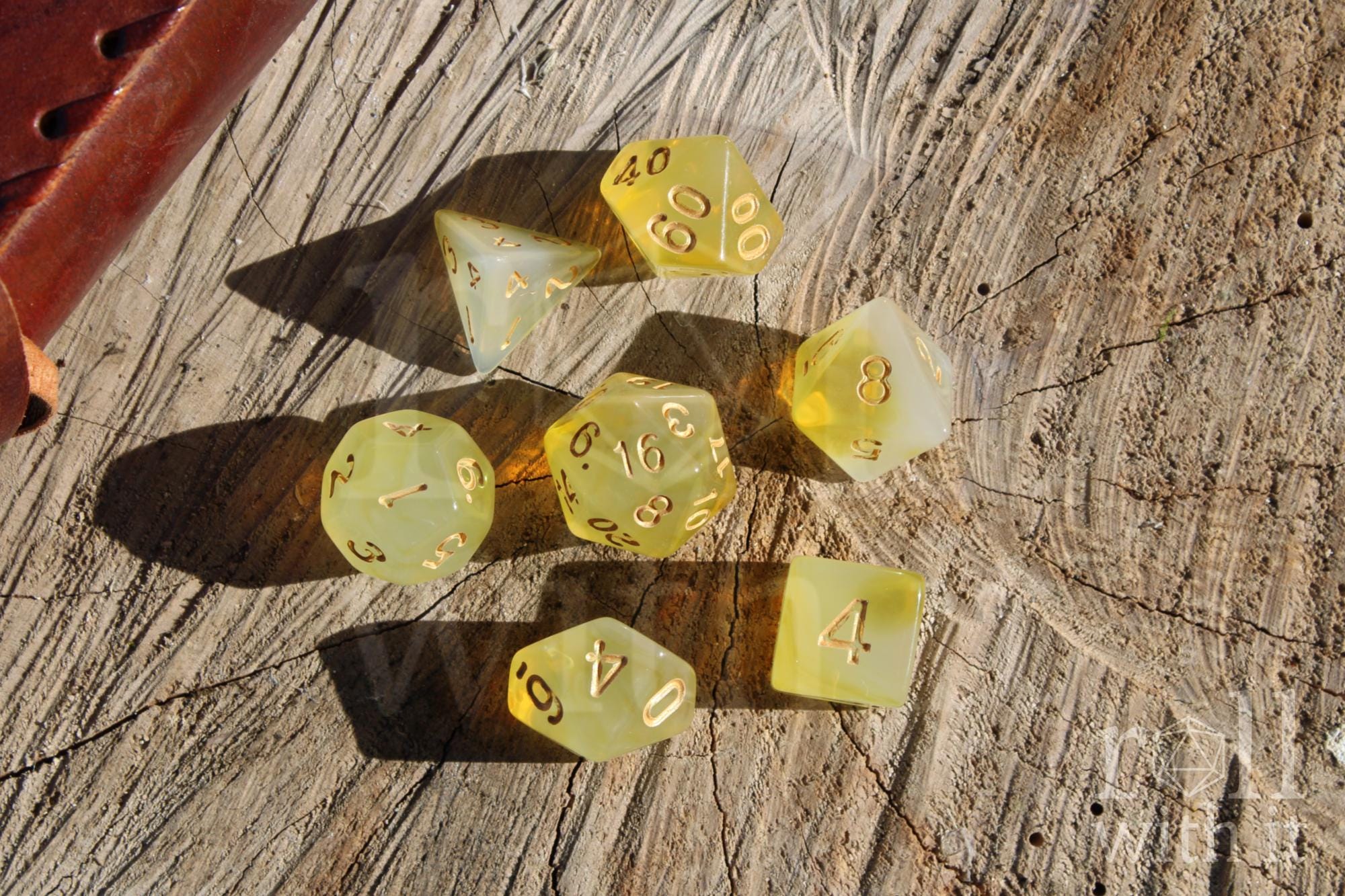 Set of translucent sherbet yellow polyhedral roleplaying dice with gold numbers on a wooden surface.