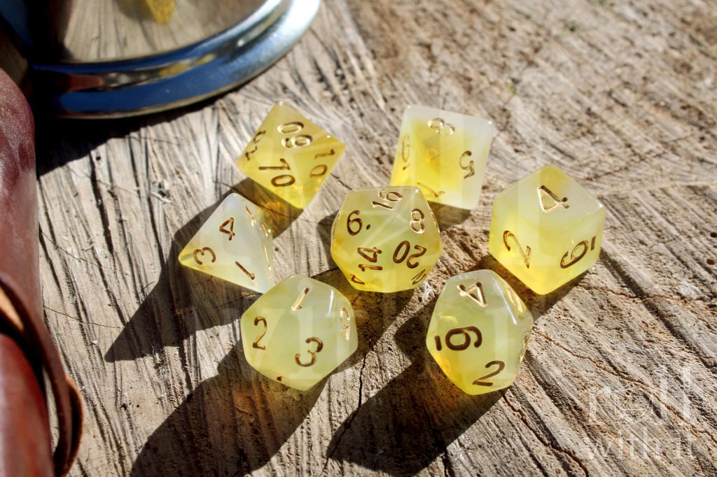 Set of translucent lemon yellow polyhedral roleplaying dice with gold numbers on a wooden surface.