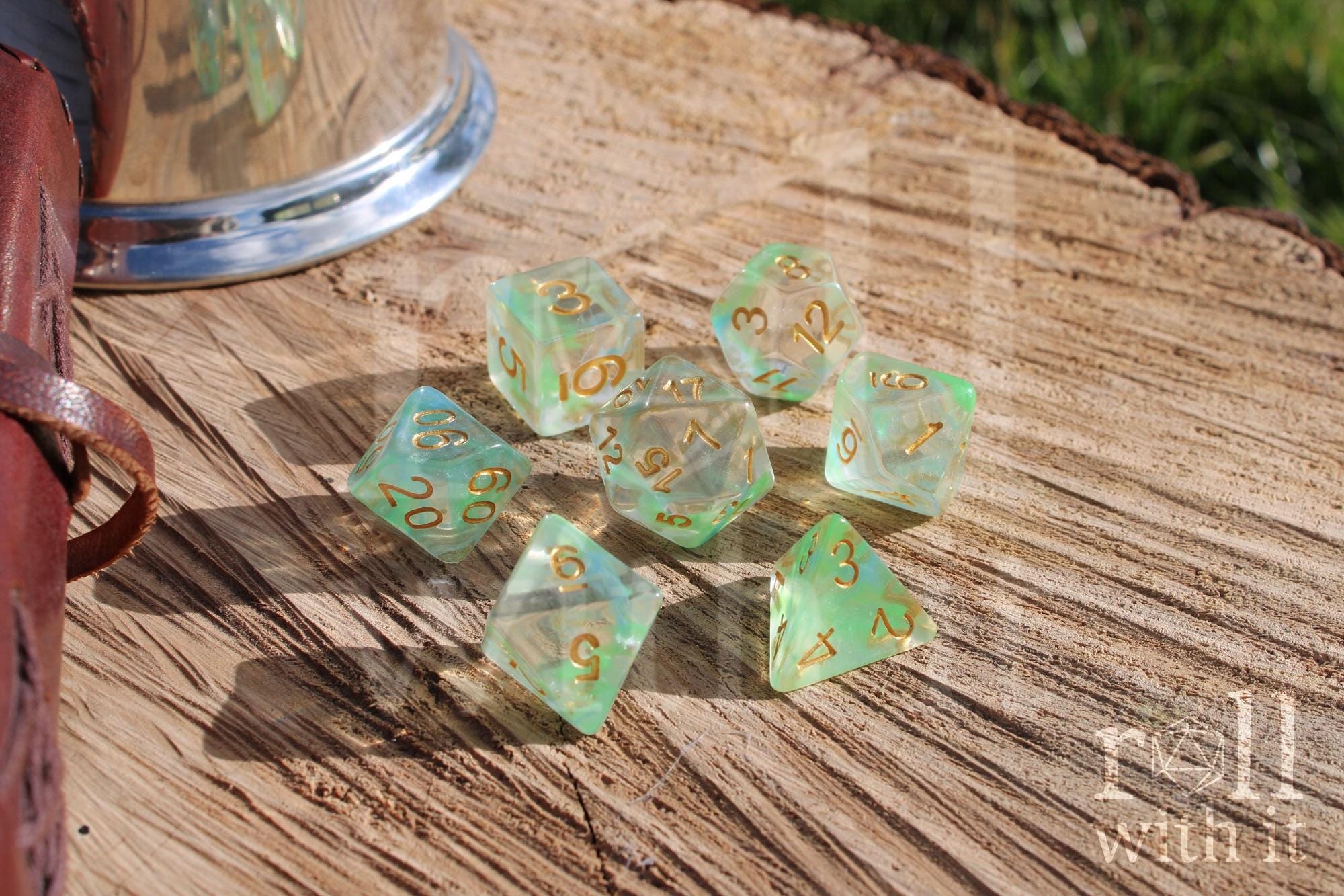 Set of green and pale blue clear polyhedral DND dice with gold numbers on a wooden surface