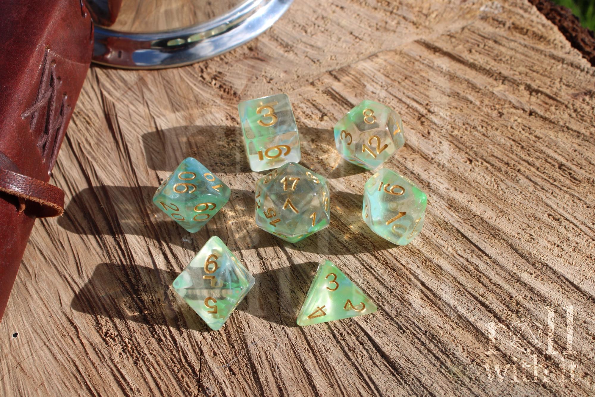 Set of green and pale blue clear polyhedral DND dice with gold numbers on a wooden surface