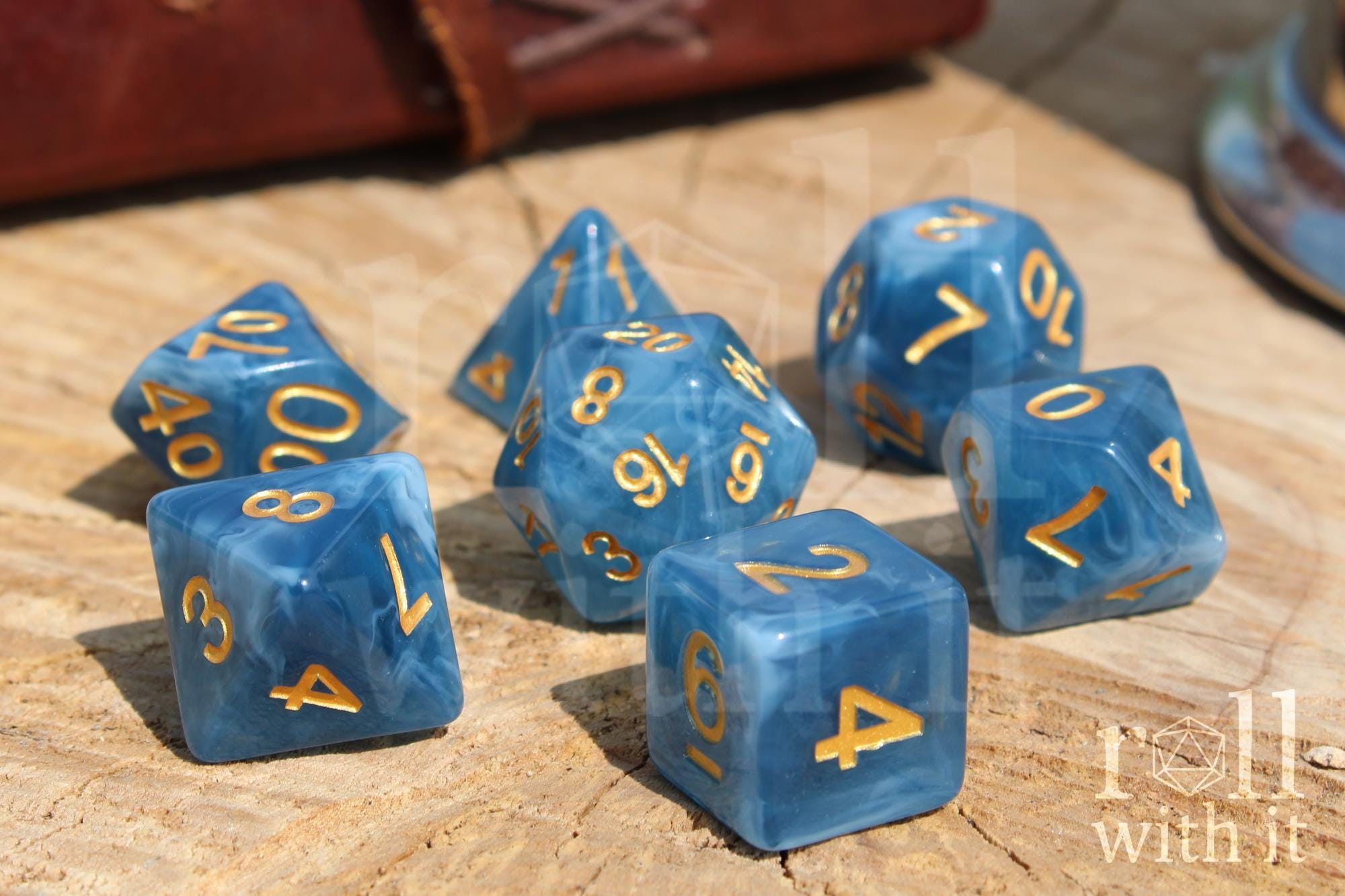 Set of jade blue translucent polyhedral roleplaying dice with gold numbering on a wooden base.
