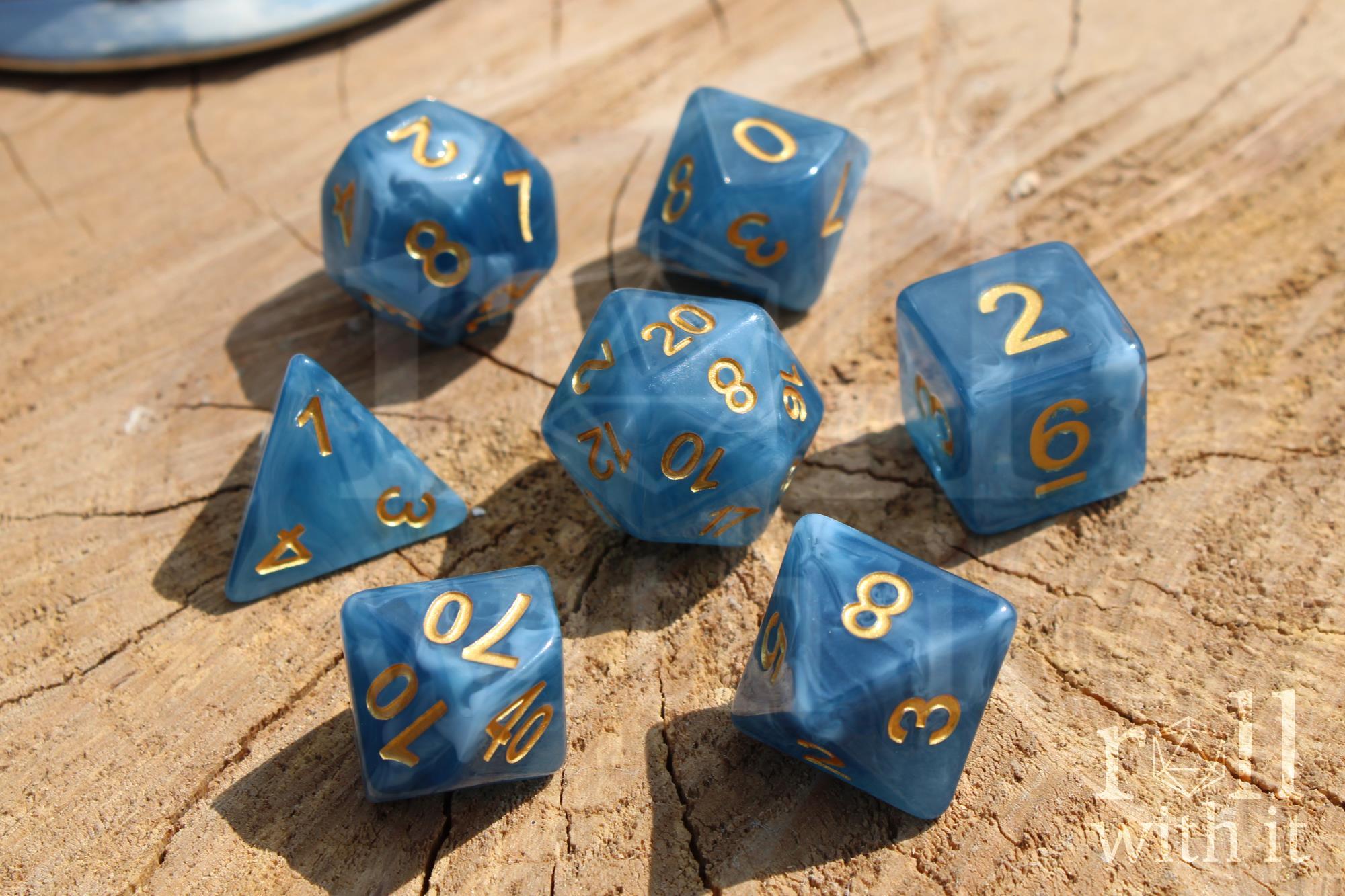 Set of jade blue translucent polyhedral roleplaying dice with gold numbering on a wooden base.