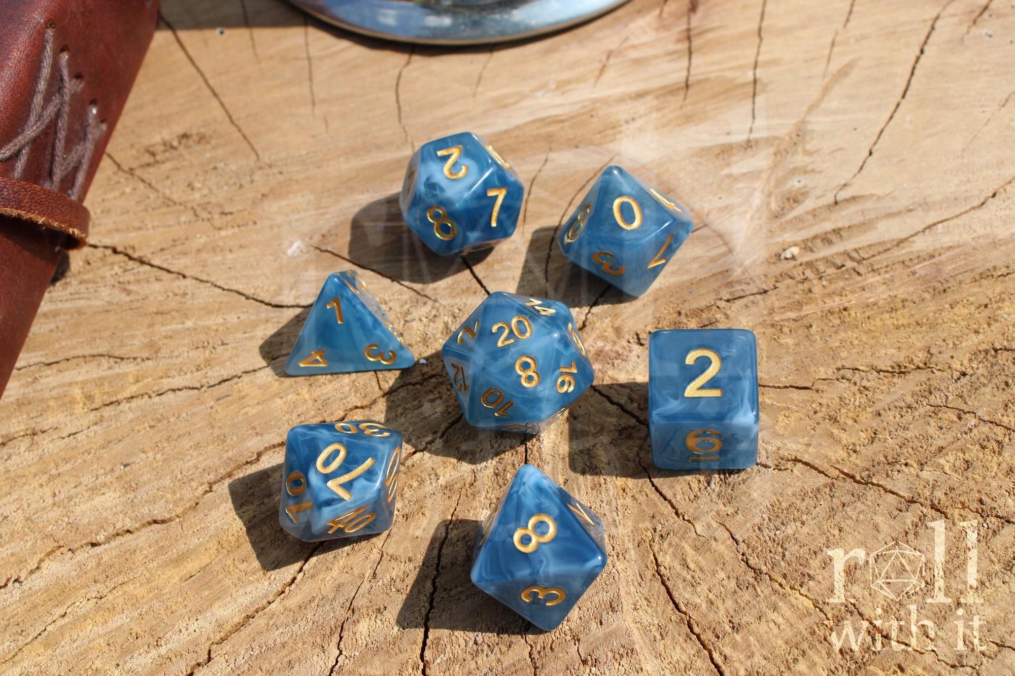 Set of jade blue translucent polyhedral roleplaying dice with gold numbering on a wooden base.