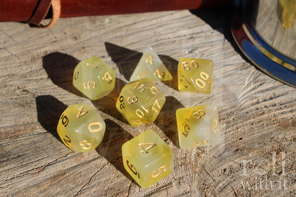 Set of translucent sherbet yellow polyhedral dice with gold numbers on a wooden surface.