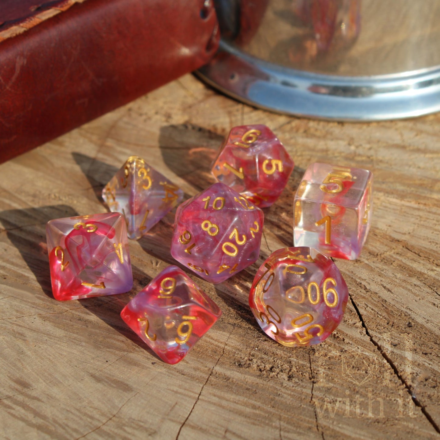 Set of 7 cute girly rose flower pink and clear polyhedral dice with gold numbers on a wooden surface.