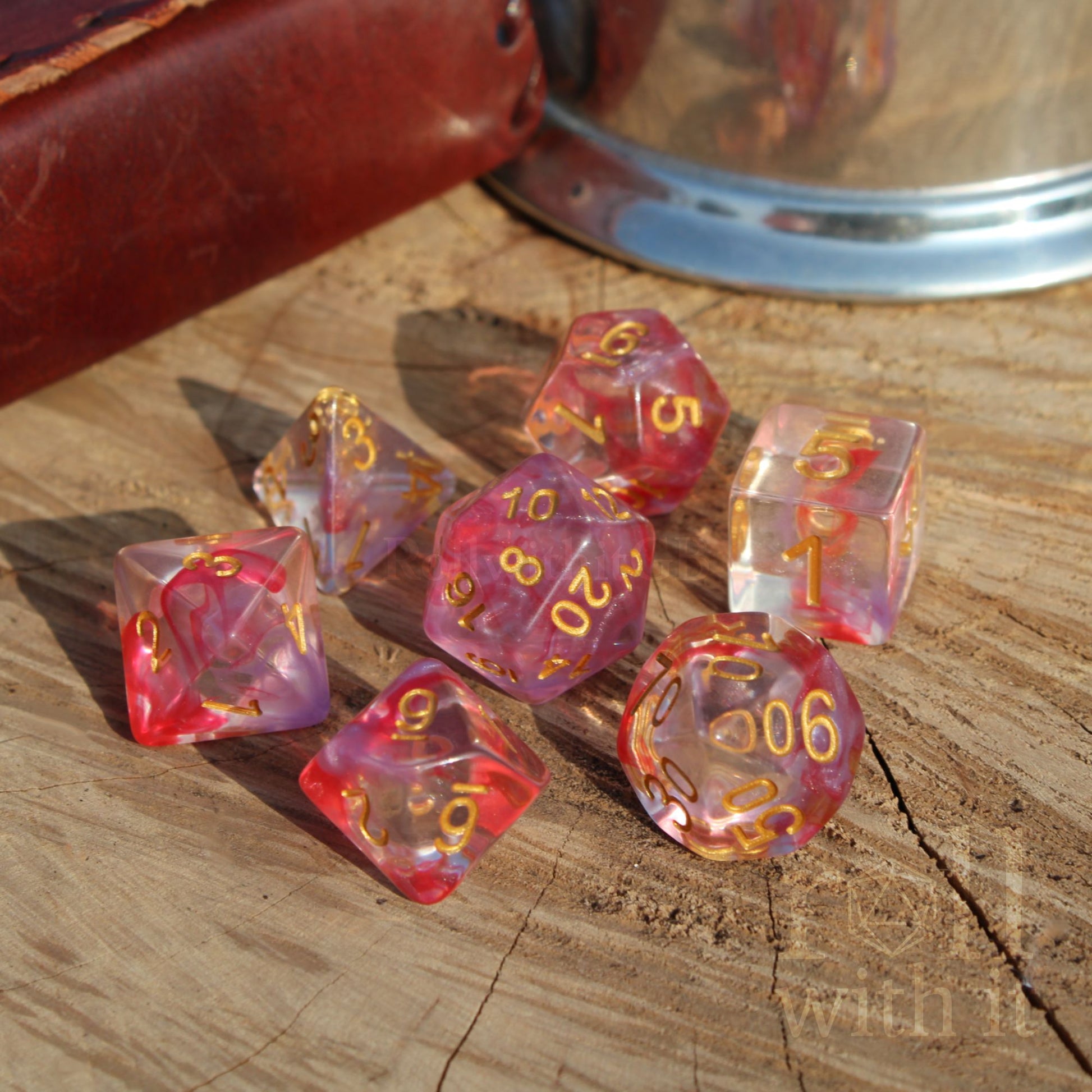 Set of 7 cute girly rose flower pink and clear polyhedral dice with gold numbers on a wooden surface.