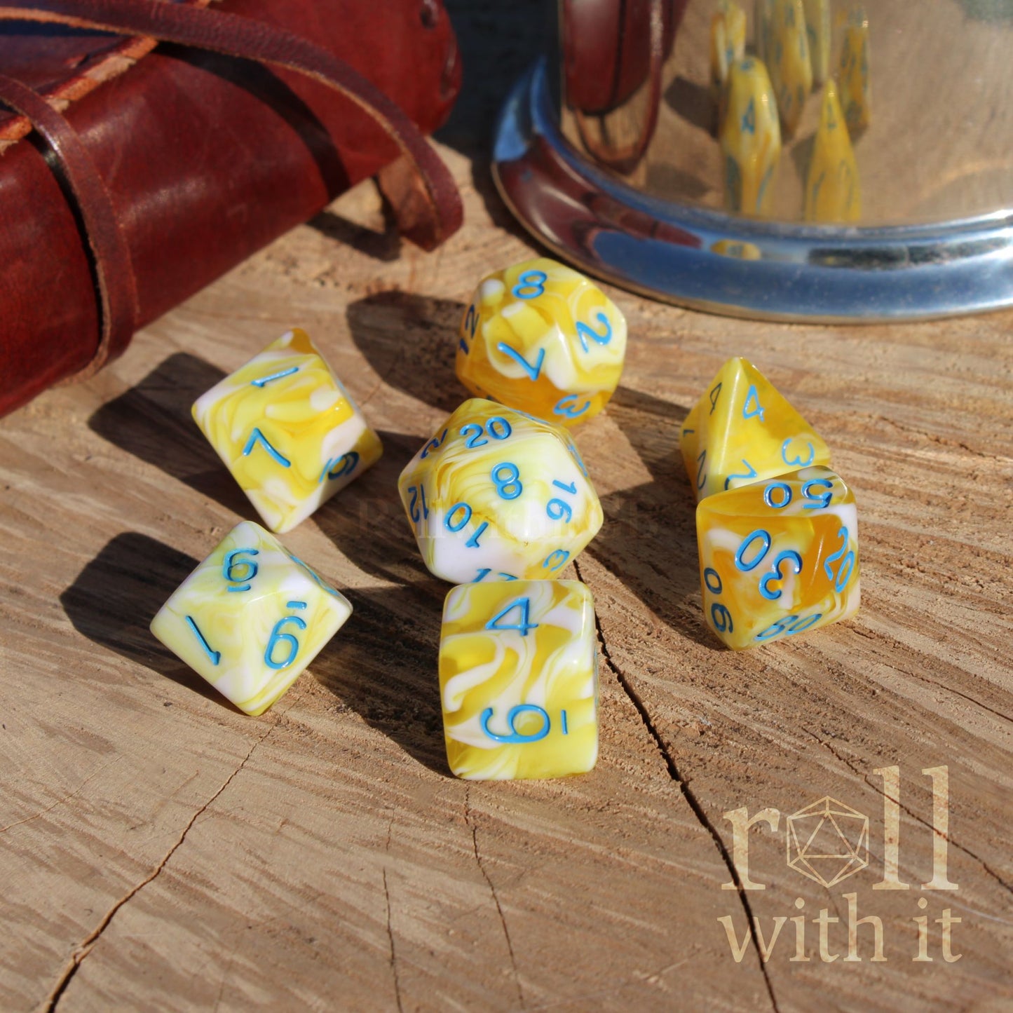 Yellow and white polyhedral dice with blue numbers on a wooden surface, featuring the 'roll with it' logo.