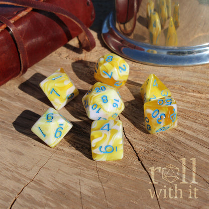 Yellow and white polyhedral dice with blue numbers on a wooden surface, featuring the 'roll with it' logo.