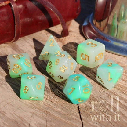 Set of green pale white polyhedral dice with gold numbers on a wooden surface, featuring 'roll with it' branding.