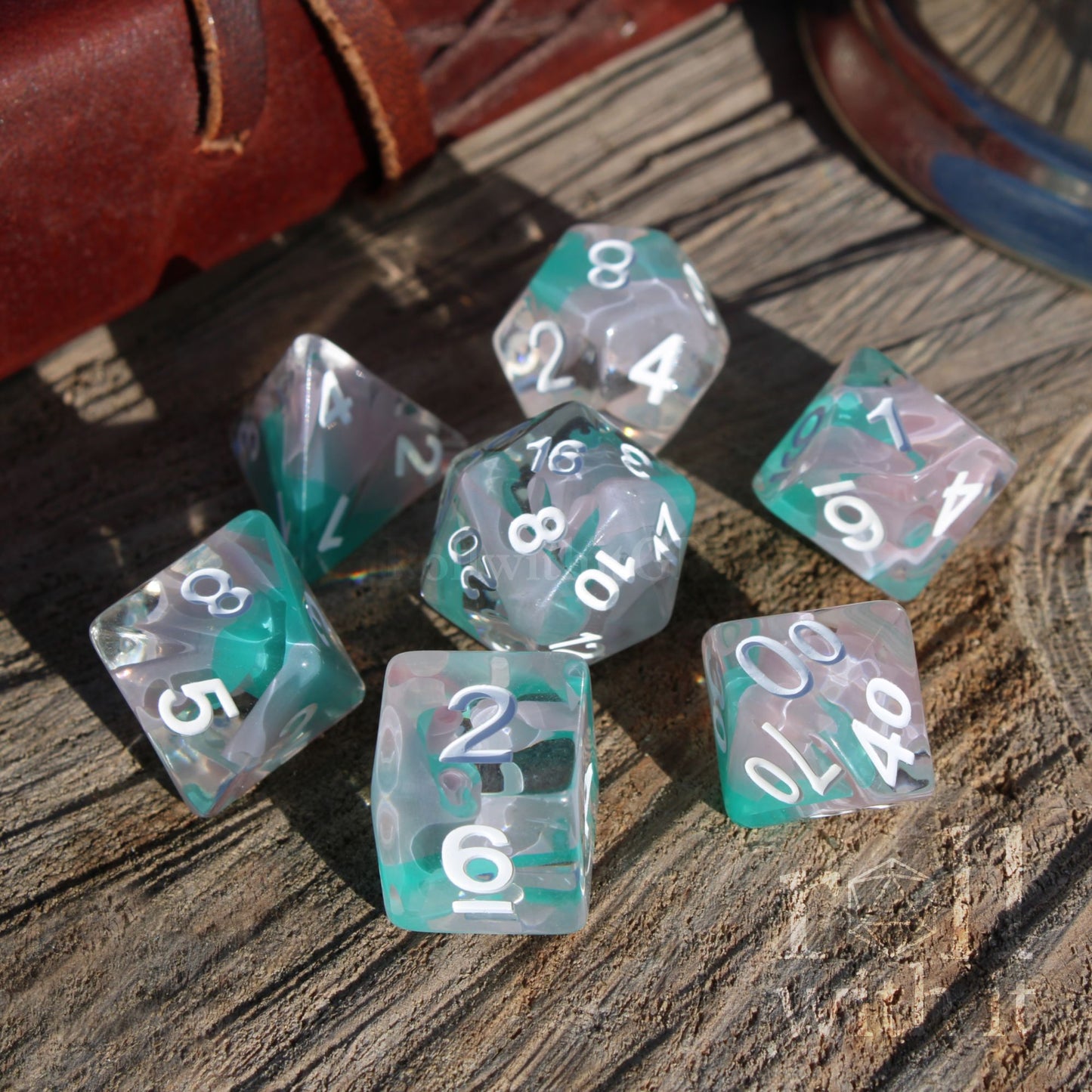 Set of teal and clear bright shiny polyhedral dice with white numbers on a wooden surface
