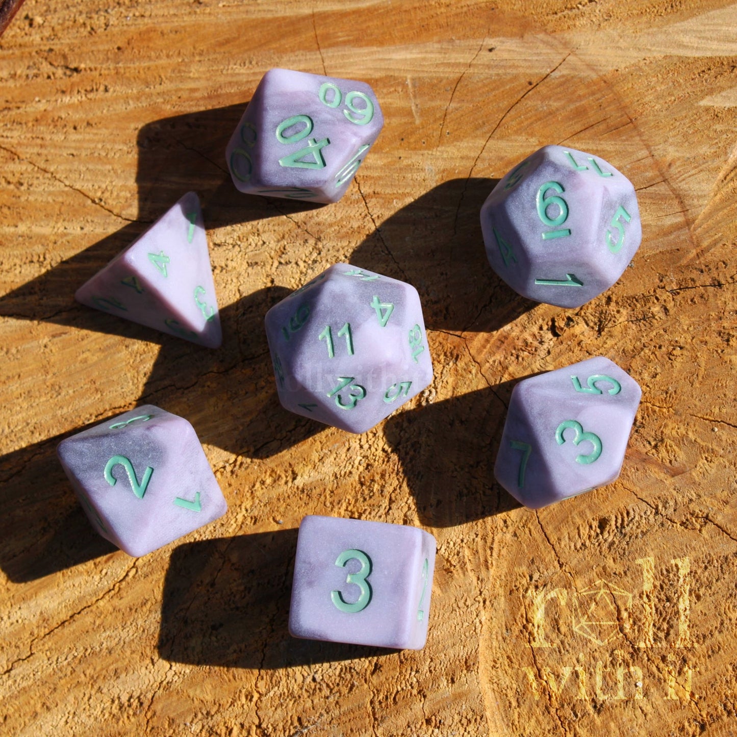 A set of 7 pale lilac matte purple polyhedral dice on a wooden surface