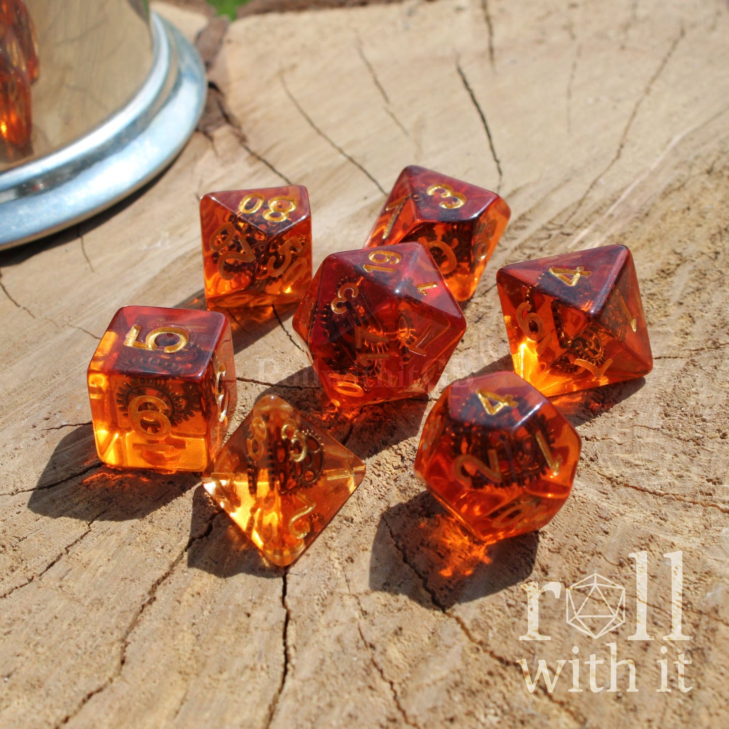 Set of bright shiny interesting artificer themed amber-colored and cog machine filled dice with 'roll with it' logo on a wooden surface