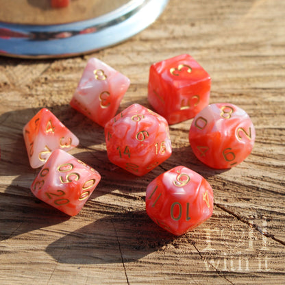 Set of red pink marble swirl polyhedral dice with gold numbers on a wooden surface