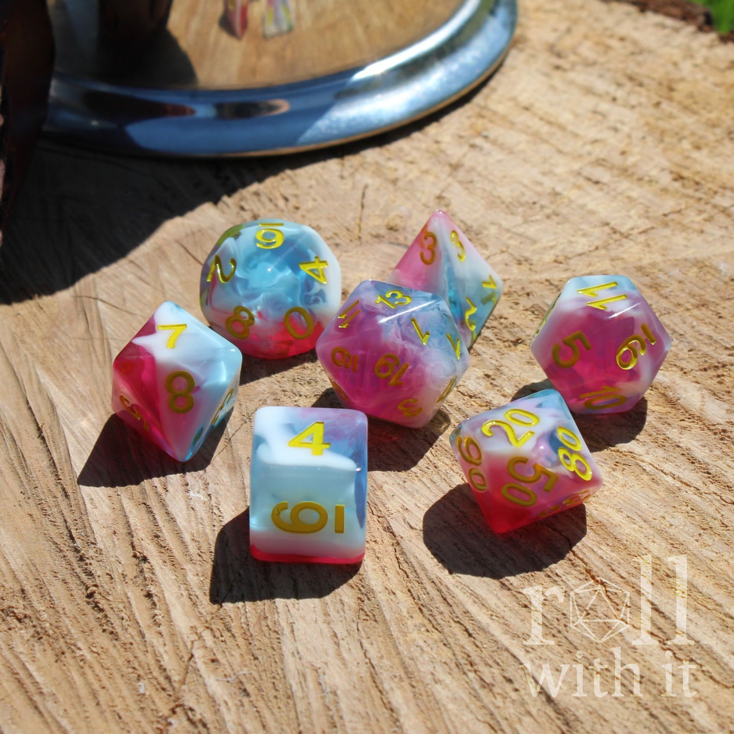 Set of colorful mixed swirling pink white blue polyhedral dice on a wooden surface with 'roll with it' text.