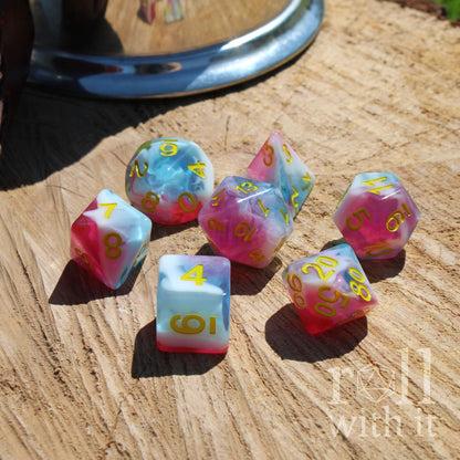 Set of colorful mixed swirling pink white blue polyhedral dice on a wooden surface with 'roll with it' text.