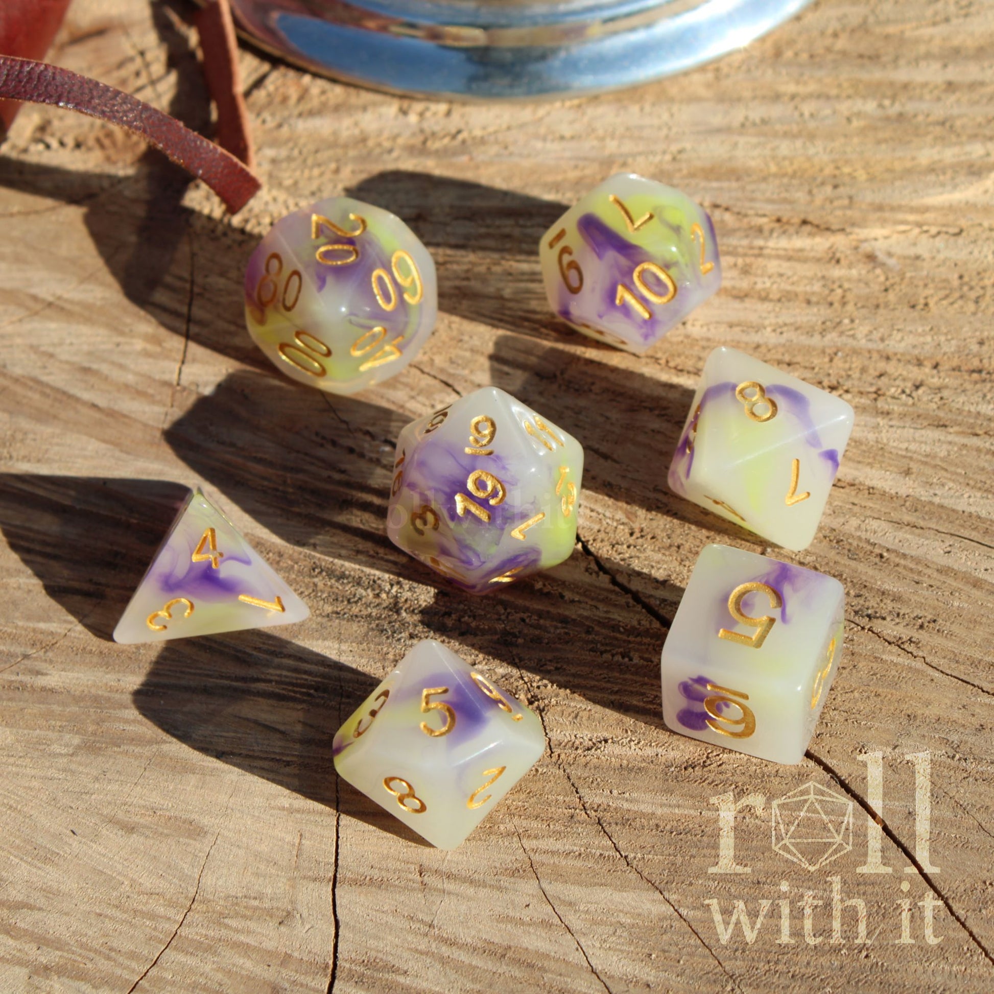 Set of dice with purple green colour and gold numbers on a wooden surface, featuring 'roll with it' branding.