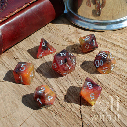 Set of polyhedral burnt orange dark glittery mixed colour dice on a wooden surface with a leather-bound book and metal tray in the background.
