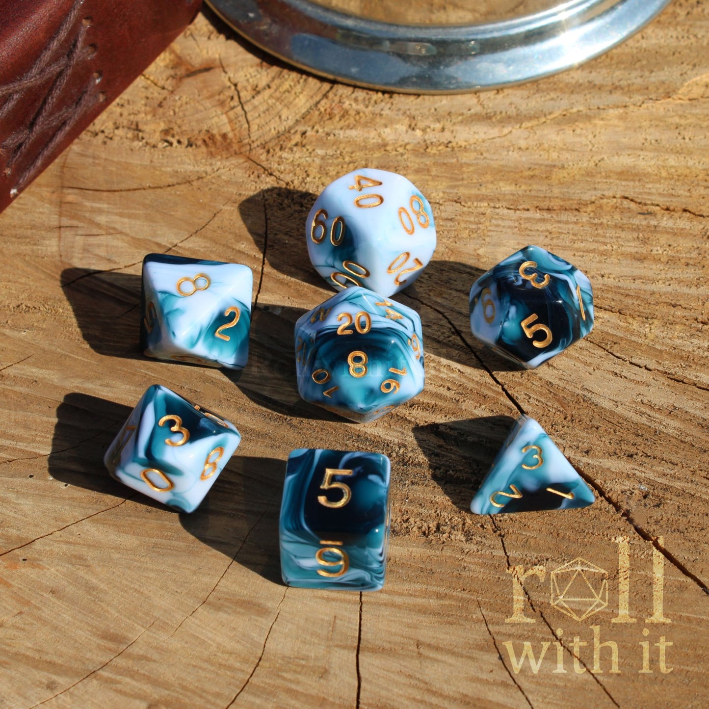Set of mixed blue and white dice with gold numbers on a wooden surface, featuring 'roll with it' logo.