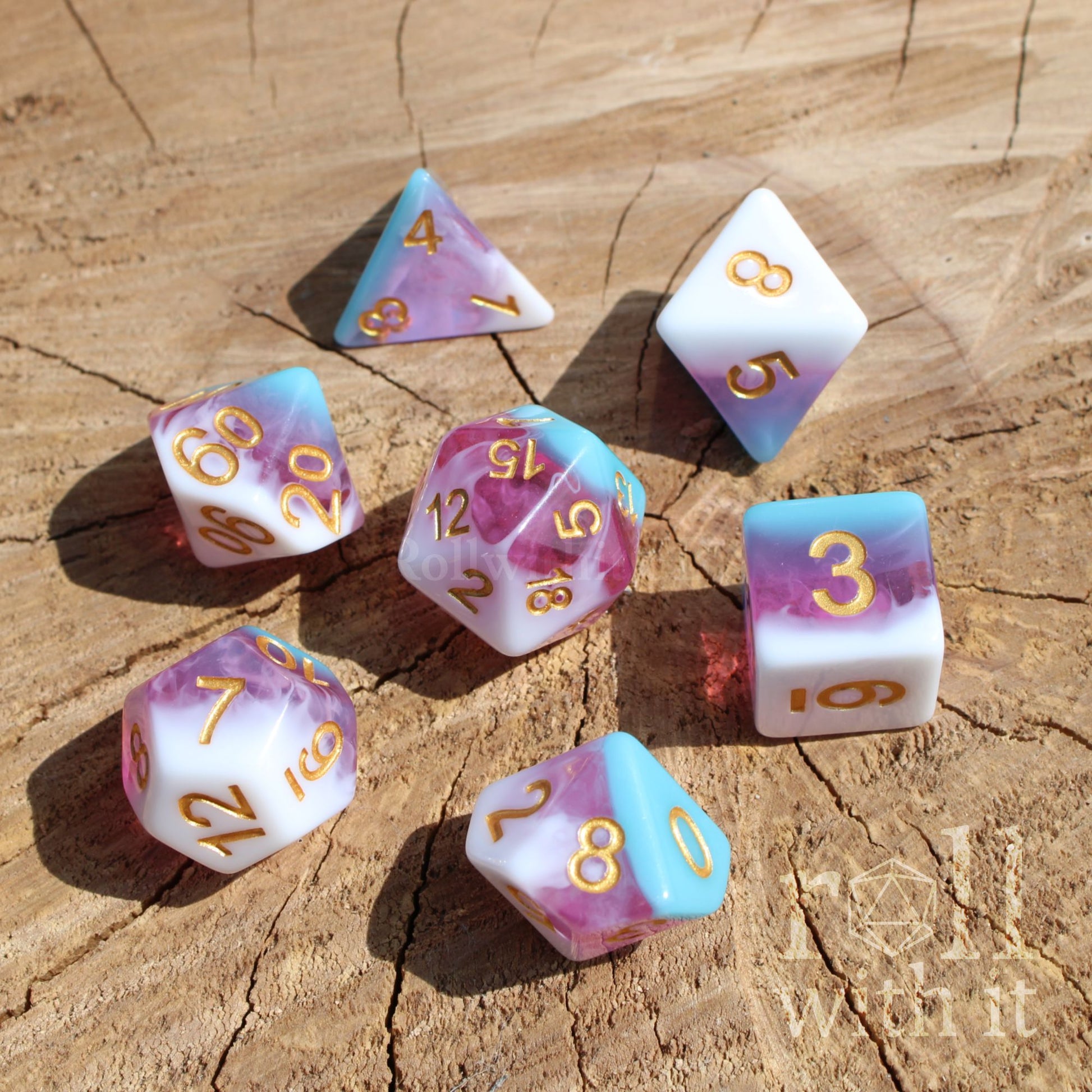 Set of colorful layered mixed pink white blue polyhedral dice with gold numbers on a wooden surface