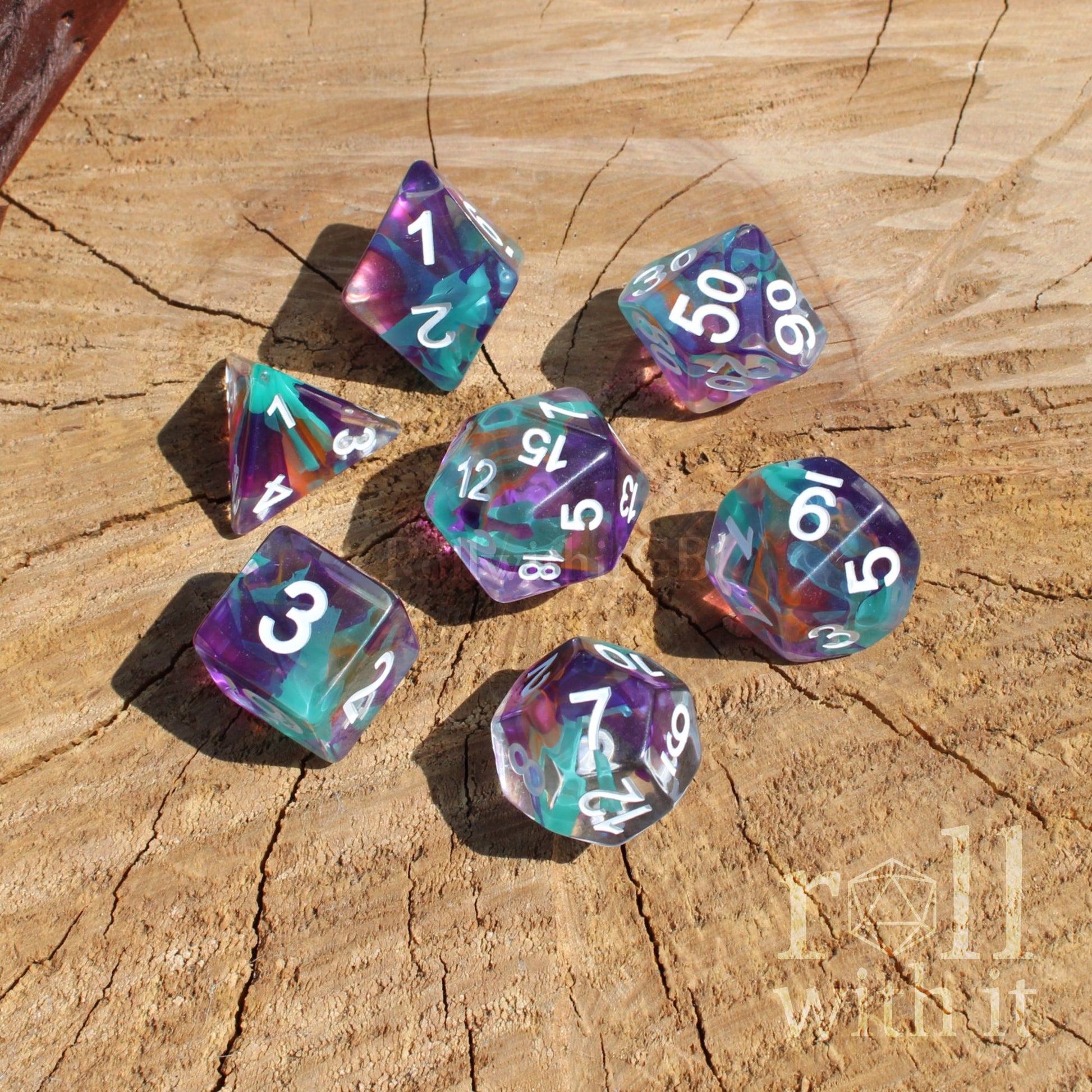 Set of colorful mixed rainbow cool purple turquoise polyhedral diceset on a wooden surface with 'roll with it' branding.