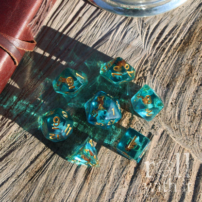 Set of teal ocean blue polyhedral dice with gold numbers and a fish inside on a wooden surface