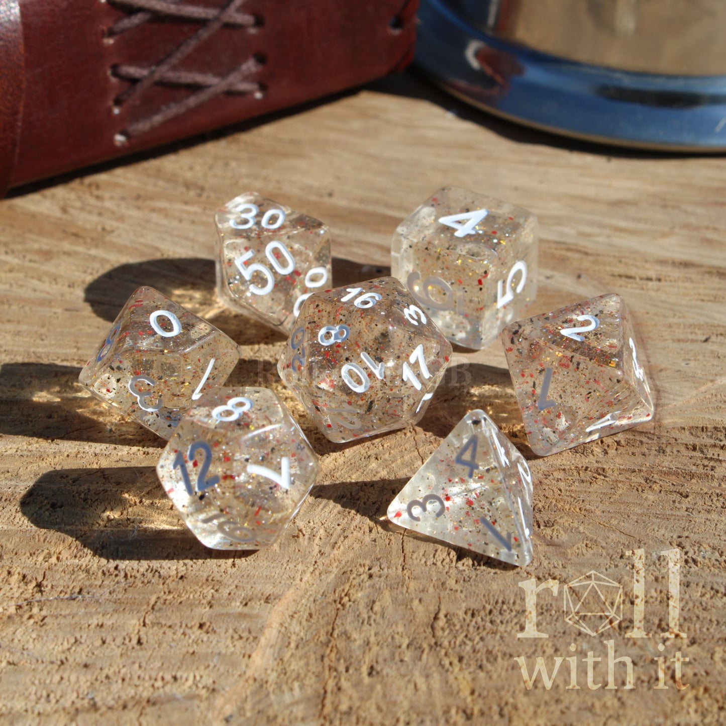 Clear speckled orange black dice set with numbers on a wooden surface, featuring the 'roll with it' logo.
