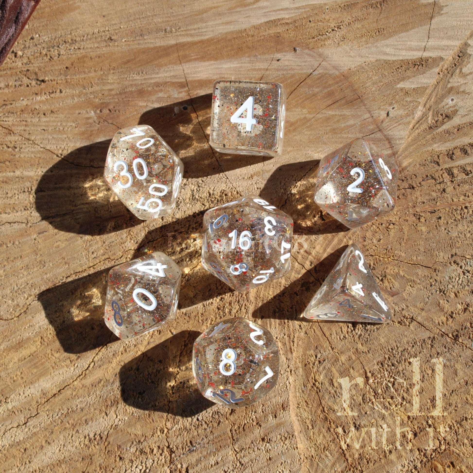 Clear dice with fish food inspired glitter speckles and white numbers on a wooden surface, featuring the brand 'roll with it'