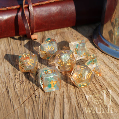 Set of dice with orange glitter filled teal swirling design and gold numbers on a wooden surface with 'roll with it' branding.