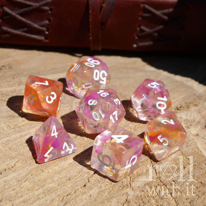 Set of colorful pink orange white numbers polyhedral dice on a wooden surface with 'roll with it' branding.