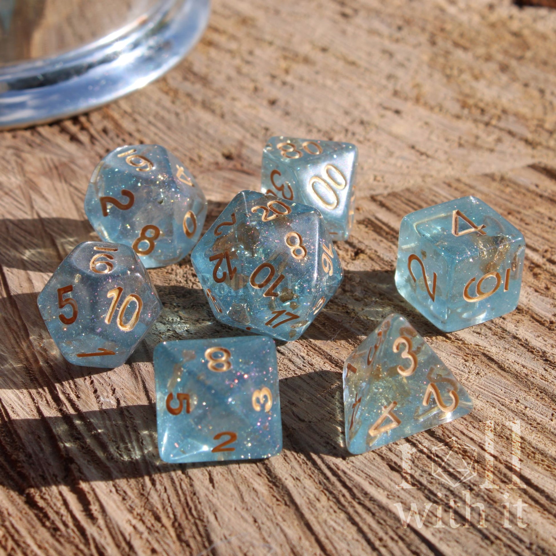 Set of clear glittery reflective blue polyhedral dice with pale gold numbers on a wooden surface