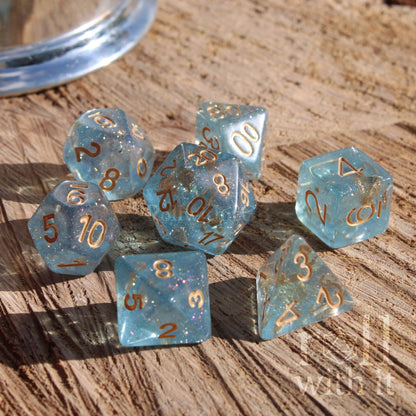 Set of clear glittery reflective blue polyhedral dice with pale gold numbers on a wooden surface