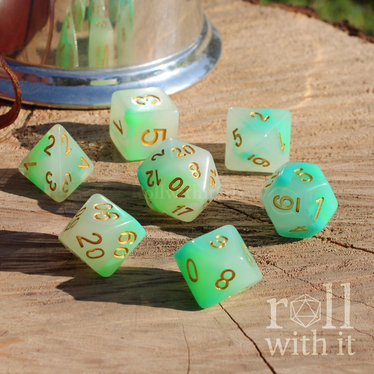 Set of pale white green dice with gold numbers on a wooden surface, featuring 'roll with it' logo.