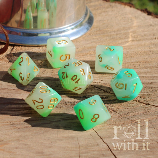 Set of pale white green dice with gold numbers on a wooden surface, featuring 'roll with it' logo.