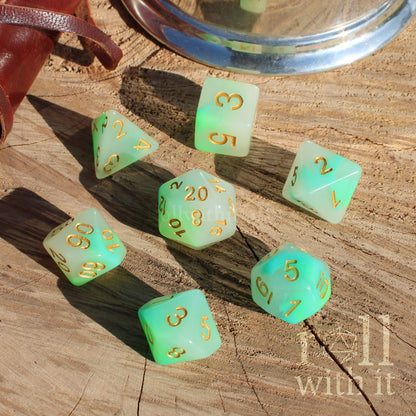 Set of pale lettuce green and white mixed polyhedral dice with gold numbers on a wooden surface