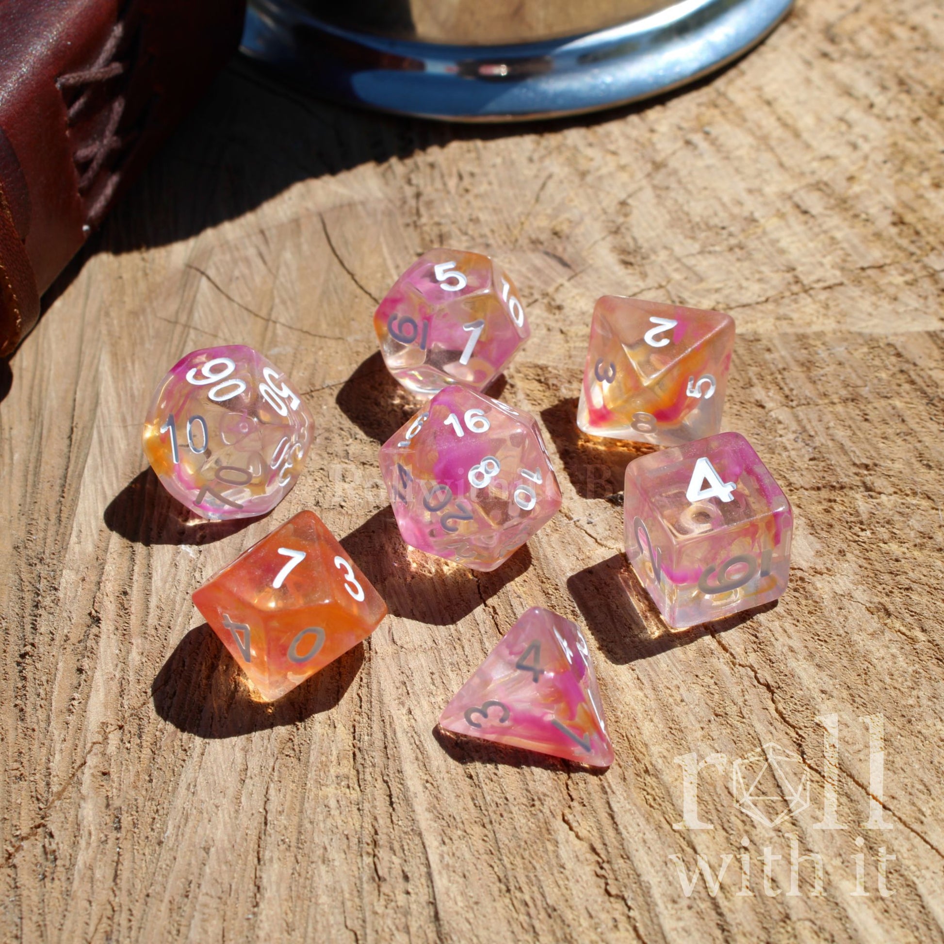 Set of colorful pale pink orange clear polyhedral dice on a wooden surface