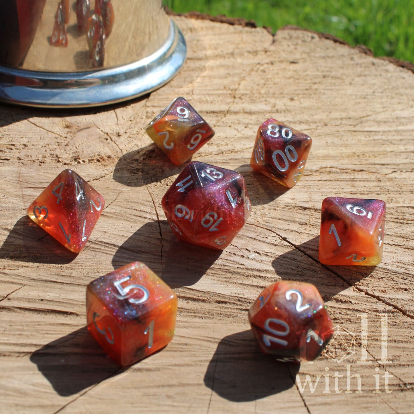 Set of colorful orange brown yellow polyhedral dice on a wooden surface with a metallic cup in the background.