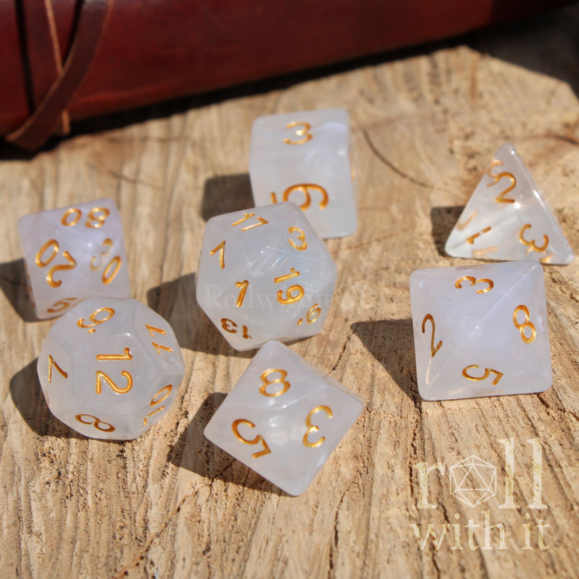 Set of white polyhedral dice with gold numbers on a wooden surface, featuring 'roll with it' branding.